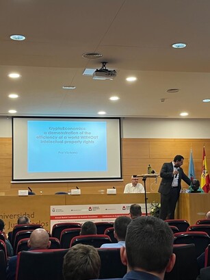 A man gives a presentation on "KryptoEconomics" from a conference stage.