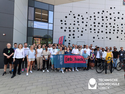 Gruppenfoto aller Teilnehmenden Über 50 lächelnde Personen stehen vor einer Fassade und halten eine Beachflag hoch