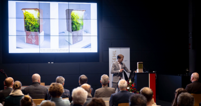 Ein Mann steht vorne, vor ihm Publikum, er zeigt eine Präsentation