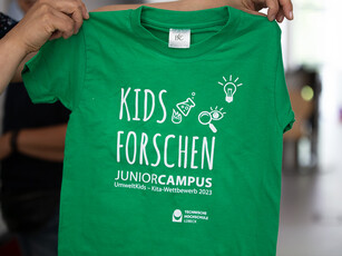 T-Shirts für die Kinder Ein grünes T-Shirt auf dem "Kids Forschen JuniorCampus" steht