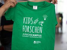Ein grünes T-Shirt auf dem "Kids Forschen JuniorCampus" steht