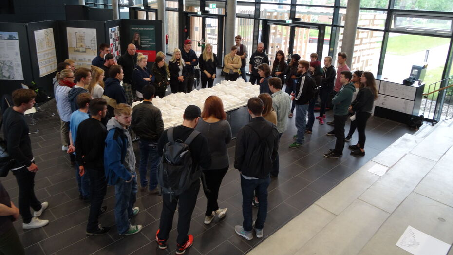 Große Gruppe Studierende versammelt sich um ein weißes Stadtmodell im Foyer.
