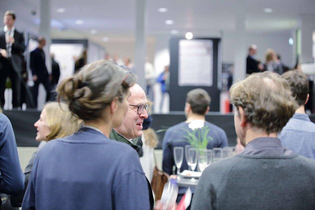 Gäste im angeregten Gespräch auf der Vernissage, im Hintergrund Sektgläser.