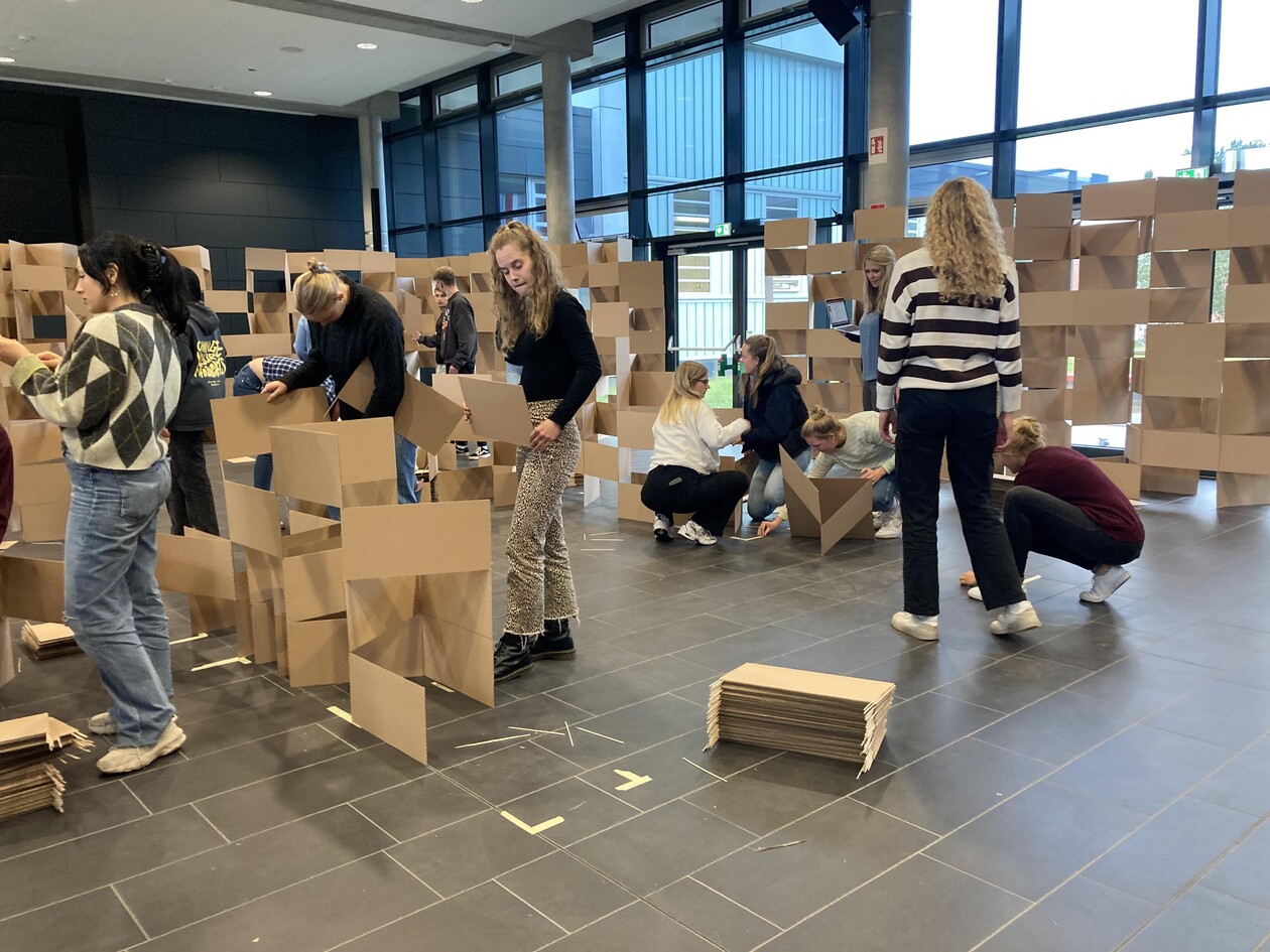 Gruppe von Studierenden steckt Pappteile zusammen und baut eine Raumstruktur.