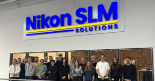 Besuchergruppe posiert vor dem großen Nikon SLM Solutions Wandlogo.