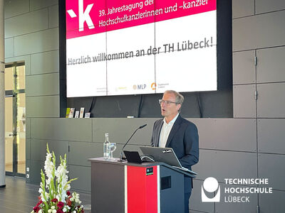 Staatssekretär steht am Pult mit Präsentation an Leinwand
