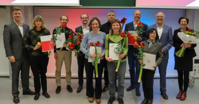 Gruppenfoto einer Preisverleihung: Menschen halten rote Blumen und Urkunden.
