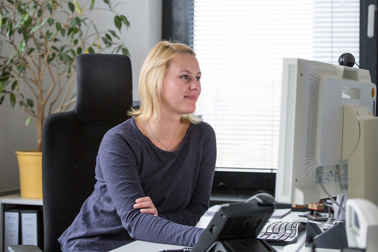 Frau sitzt im Büro an einem Schreibtisch mit zwei Monitoren