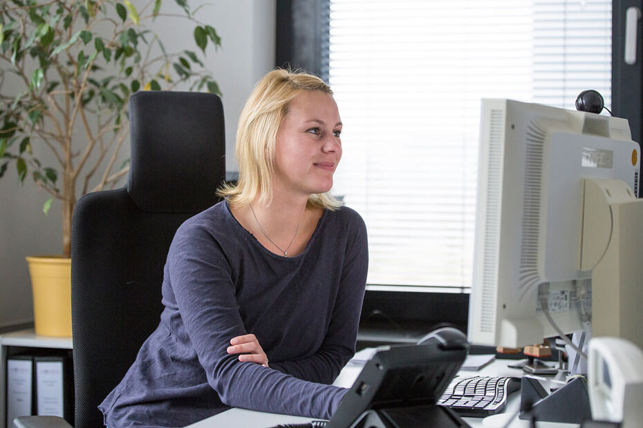 Frau sitzt im Büro an einem Schreibtisch mit zwei Monitoren