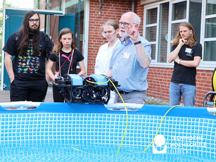 Vorführung Unterwasserroboter Ein Mann zeigt einen Roboter, der auf der Kante eines Pools steht.