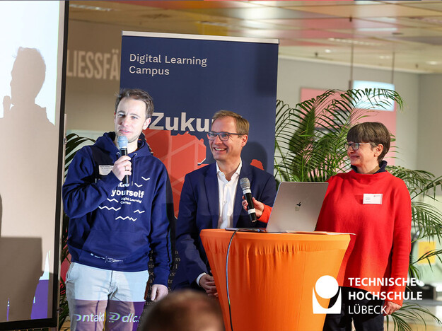 Eröffnungsrede zum Launch der Digitial Learning Plattform Drei Personen stehen am Rednerpult und zwei halten Mikrofon