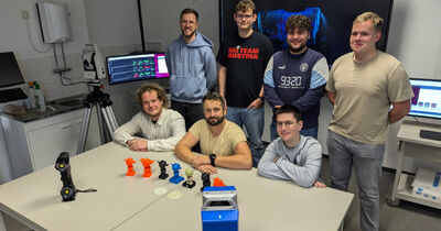 Gruppe von Studierenden und Dozenten der Technischen Hochschule Lübeck und der Hochschule Neubrandenburg, umgeben von 3D-Druck-Modellen und moderner Messtechnik während eines interdisziplinären Workshops zu 3D-Druck und Industrievermessung.
