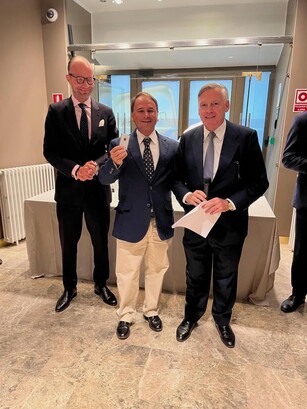 Three men in suits smile for a photo; one proudly holds up a small award.