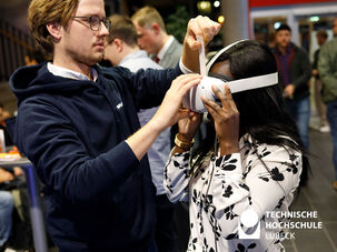 Mann hilft einer Frau eine VR Brille aufzusetzen