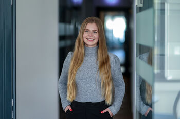 Lächelnde junge Frau mit langen blonden Haaren im Büroflur.