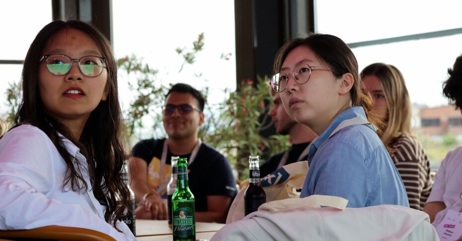 Zwei Teilnehmerinnen mit Brille sitzen an einem Tisch und hören zu