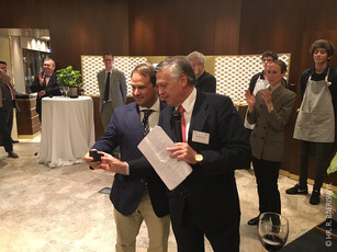 A presenter shows an award to a man in a navy blazer at a reception.