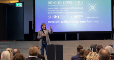 Eine Frau steht vor einer Präsentation und streckt ihre Hand in Richtung Publikum