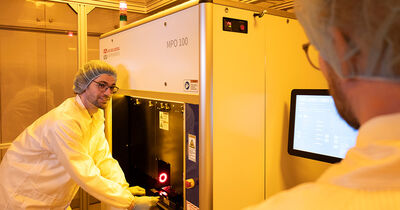 Gregor Knoll steht vor dem 3D-Drucker und positioniert das Deckglas mit dem aufgetragenen Polymer.