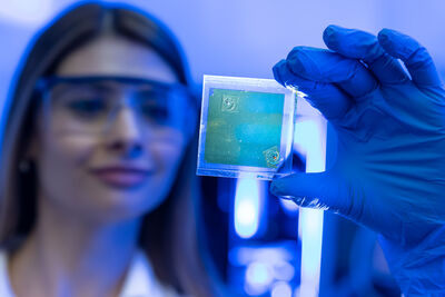 Forscherin mit Schutzbrille hält eine transparente Dünnschicht-Solarzelle.