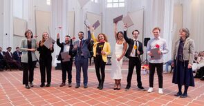 Absolvent*innen halten ihre Mappen in die Luft und freuen sich über den Applaus.