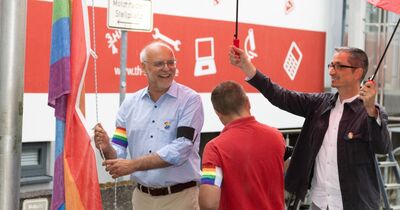 Ein Mitarbeiter hält zwei Regenschirme, während Jochen Abke die Flagge hisst.