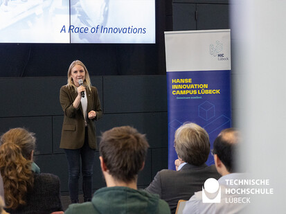 Amtsträgerin hält Eröffnungsrede für den Hanseatic Hackathon Frau hält Mikrofon in der Hand und spricht zum Publikum