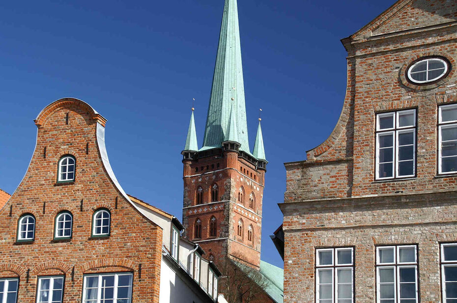 Turm der St.-Petri-Kirche in Lübeck zwischen historischen Backsteingiebeln der Altstadt vor blauem Himmel
