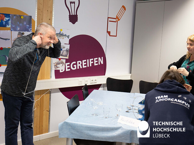 Zwei Fäden sind außen an einem Kleiderbügel befestigt und ein Mann hält die Fadenenden an seine Ohren