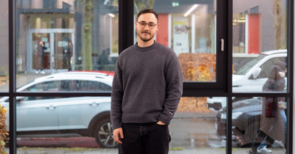 Thorleif Harder steht in grauem Pullover vor einer großen Fensterfront.