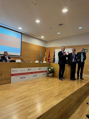Three men stand on stage for an awards presentation while another is seated.