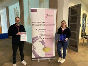Zwei Studierende stehen neben Plakat und halten Urkunde in den Händen