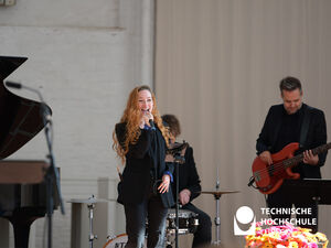 Eine Frau mit langen Haaren singt in ein Mikro, neben ihr ein Bassist und im Hintergrund ein Schlagzeuger