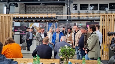 Eine Gruppe von Menschen steht gemeinsam im Messebereich, einige unterhalten sich.