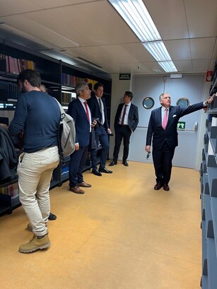 A man in a suit shows a group of men the shelves in a library archive room.