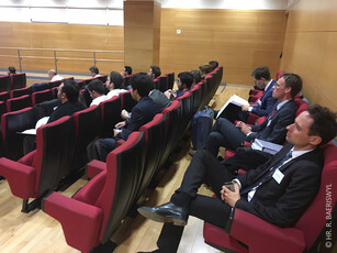 A side view of an audience of men in suits listening in a lecture hall.