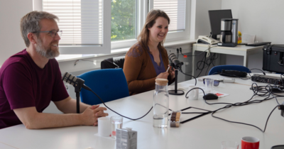 Ein Mann und eine Frau mit Podcastmikrophonen im Gespräch