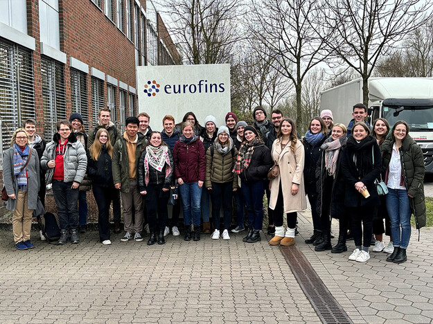 Besuch des Eurofins Campus Studierende stehen vor einem Schild mit eurofins Schriftzug