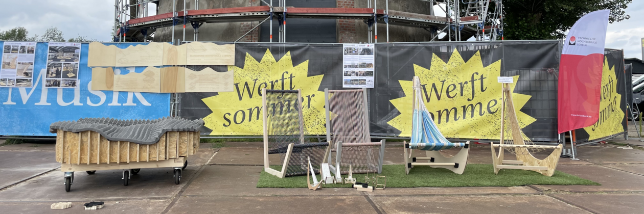 Pappmöbel Outdoor-Ausstellung von kreativen Möbelstücken und Holzobjekten vor Werbebannern und Bauzaun.