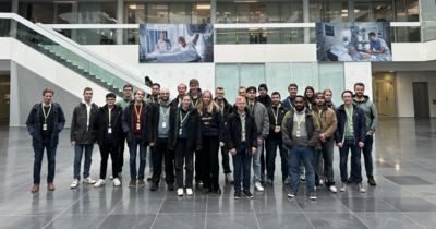 Große Gruppe steht im Atrium eines modernen Gebäudes mit Treppenaufgang.