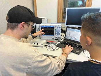 Zwei Hörakustik-Studenten analysieren im Labor der TH Lübeck Audiosignale an einem Oszilloskop und einem Laptop mit Messsoftware.