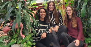 Drei Frauen sitzen auf einer Bank in einem Raum von vielen großen grünen Pflanzen umgeben