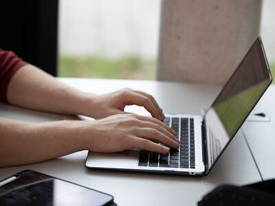 Auf dem Bild sind zwei Hände zu sehen die einen Laptop bedienen