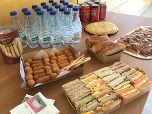 A catering table with sandwiches, croquettes, ham, bread, and drinks.
