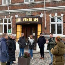 9 Personen stehen vor Hotel Vinhuset und eine erklärt etwas