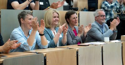 MINT-Schulen-Akkreditierung_2 Ausschnitt eines Hörsaals. Im Vordergrund sitzen vier Personen nebeneinander und klatschen.