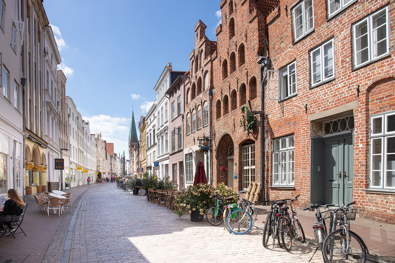 Sonnige Altstadtstraße mit Backsteinhäusern, Cafés und geparkten Fahrrädern.