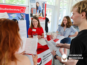 Studienberatungsstand Eine Frau in einem roten T-Shirt lächelt, erklärt Studieninteressierten, was sie an der TH Lübeck studieren können