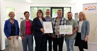 MINT-Schulen-Akkreditierung_4 Mehrere Personen halten eine Urkunde in der Hand und lächeln.