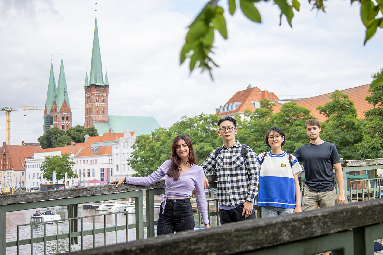 Four students on a bridge in front of the historic Lübeck skyline.